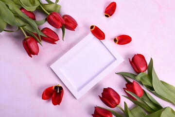Red tulips bouquet and white photo frame on pink background. Valentine's Day, Woman's Day and Mother's Day concept. View from the top 
