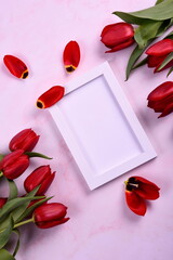 Red tulips bouquet and white photo frame on pink background. Valentine's Day, Woman's Day and Mother's Day concept. View from the top 