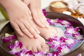 Obraz na płótnie Canvas closeup view of woman soaking her hand and feet in dish with water and flowers on wooden floor. Spa treatment and product for female feet and hand spa. orchid flowers in ceramic bowl.