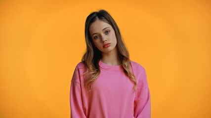 sad teenage girl in pink sweatshirt looking at camera isolated on yellow