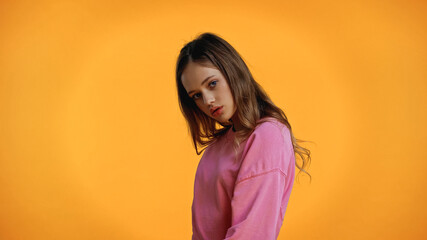 teenage girl in pink sweatshirt looking at camera isolated on yellow