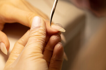 Close up of manicurist hands clipping client nails. Young woman getting manicure treatment. Clipping nails, hand care and nail care at beauty salon. Selective focus.