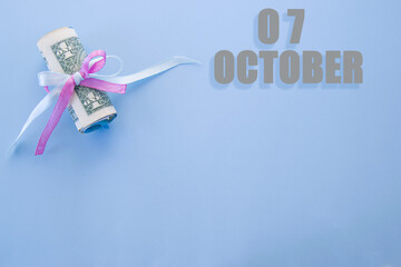 calendar date on blue background with rolled up dollar bills pinned by blue and pink ribbon with copy space.  October 7 is the seventh day of the month