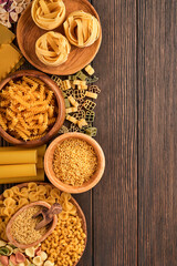 Variety of traditional italian pasta: colorful spaghetti, tagliatelle, farfalle, penne, ptititm, noodle, fusilli, cannelloni on an old wooden background. Top view with copy space.