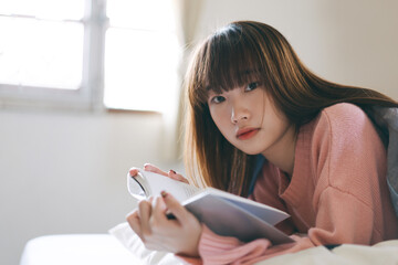 Portrait young asian cute woman teen college student reading a book at bedroom on morning.