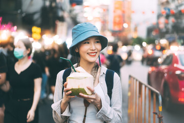Young adult asian foodie woman backpack traveller eating coconut juice at china town street food.