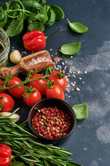 Food cooking background. Fresh rosemary, cilantro, basil, cherry tomatoes, peppers and olive oil, spices herbs and vegetables at black slate table. Food ingredients top view.