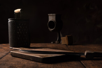 Rustic wooden table with board, knife and old corn grater, low key portrait, dark abstract background, selective focus.