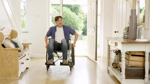 Mature Asian man in wheelchair pushing himself in hallway at home towards camera- shot in slow motion