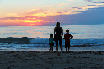 Silhouette of Mother with daughter and son watching sunrise along the beach of the Atlantic Ocean...