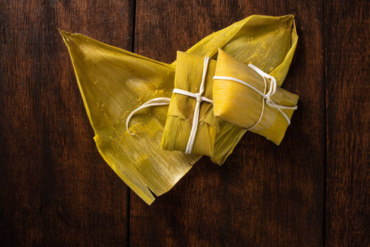 Pamonha, Brazilian corn food, called pamonha. On a rustic table with knife, low key portrait, dark abstract background, top view.