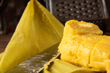Pamonha, Brazilian corn food, called pamonha. On a rustic table with knife and old corn grater, low key portrait, dark abstract background, selective focus.