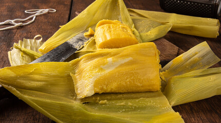 Pamonha, Brazilian corn food, called pamonha. On a rustic table with knife and old corn grater, low key portrait, dark abstract background, selective focus.
