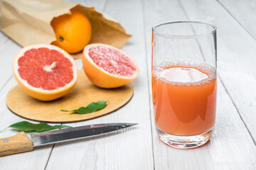 Naklejka na ściany i meble Grapefruit juice in a glass on a wooden table, fresh cut oranges in the background