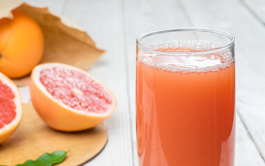 Grapefruit juice in a glass on a wooden table, fresh cut oranges in the background
