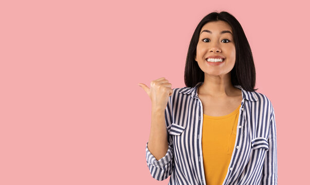 Excited asian woman pointing aside at copy space