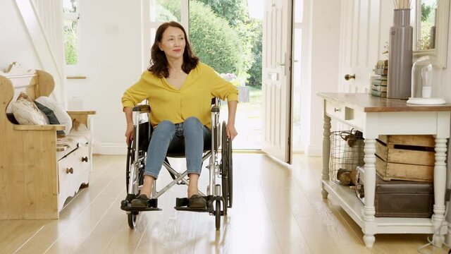 Mature Asian woman in wheelchair pushing himself in hallway at home towards camera- shot in slow motion