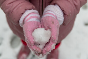 Little girl with pink coat and pink gloves holding snow outside in winter