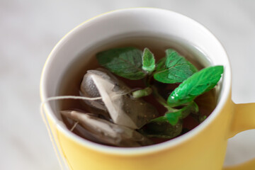 two tea bags are brewed in a yellow cup with peppermint leaves