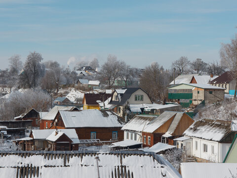 Beautiful winter houses with snow on the roof. Clear sky. Small town with private houses in the center. Smoke. Trees in the snow. Russia, Smolensk region, Roslavl.