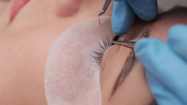 Eyelash extension procedure. The working process of professional beauty master lengthening female lashes. Fake eyelashes. Eyelashes extensions close up. Makeup artist and client in beauty salon.