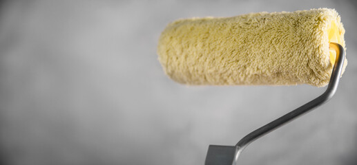 Clean fresh new paint roller for painting on gray blurred concrete background. Close up with copy empty space for text. Banner for advertising.