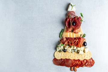 Antipasto or Italian appetizers with ham, prosciutto, salami, cheese, crackers and capers on stone background. Christmas tree Long banner format, top view