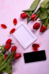 Red tulips bouquet, phone and white photo frame on pink background. Valentine's Day, Woman's Day and Mother's Day concept. View from the top 