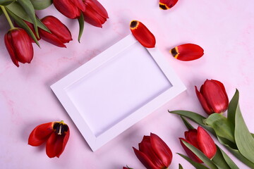 Red tulips bouquet, phone and white photo frame on pink background. Valentine's Day, Woman's Day and Mother's Day concept. View from the top 
