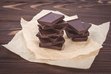 Dark chocolate pieces on a brown background of wooden boards. Sweets, candies on crumpled craft...