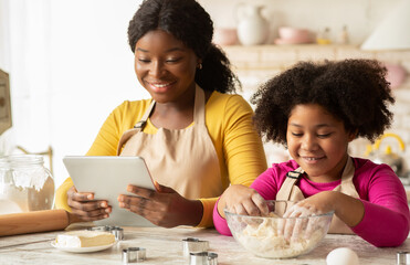 Cheerful Black Mom And Daughter Using Digital Tablet In Kitchen, Checking Recipe