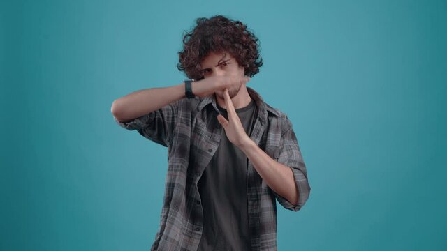Hipster crosses his hands to show his bewilderment, So far, stop.i. Curly-haired teenager. Charismatic hipsterv Studio video, Blue background, Portrait.4k