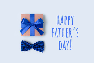 Happy Fathers Day. Festive flatlay with gift box and bow tie. Present tied with a ribbon on a blue...