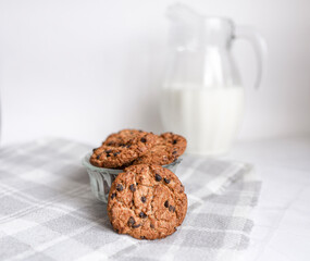 Oatmeal cookies with chocolate pieces and milk in a jug in the background. A healthy snack or breakfast at home on the table. Christmas drinks. selective focus. copy space for text