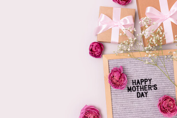Happy Mothers day. Letter board, gypsophila and rose flowers, gifts tied with ribbons on a gray background. Festive concept with copyspace.