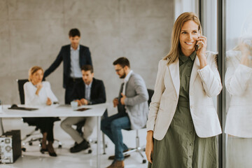 Young business woman standing in the office and using mobile phone in front of her team