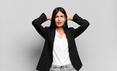 young hispanic businesswoman feeling stressed, worried, anxious or scared, with hands on head, panicking at mistake