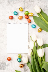 Top view of white tulips, blank calendar and colored easter eggs on concrete backgrund with copy space