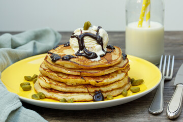 American pancakes with ice cream and chocolate sauce and pistachios on a yellow plate