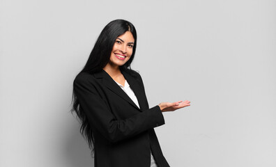young hispanic businesswoman smiling cheerfully, feeling happy and showing a concept in copy space with palm of hand