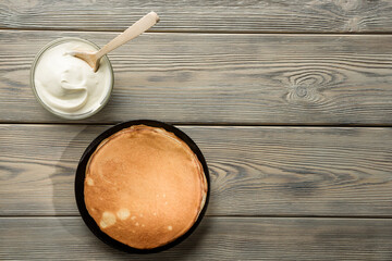 Pancakes and a cup of sour cream on a wooden table with copy space. Russian carnival.