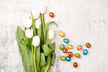 Top view of white tulips and colored easter eggs on concrete backgrund with copy space