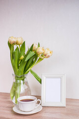 Bouquet of beautiful tulips and empty frame mock up. Copy space. International Women's Day celebration. White wall background. Scandinavian interior.