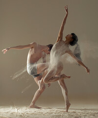 Two ballet dancers perform dance against background of white flour cloud in air.