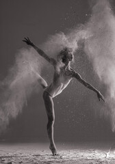 Ballerina performs arabesque pose against background of white flour cloud in air.