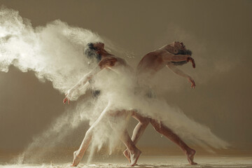 Two ballet dancers perform dance against background of white flour cloud in air.