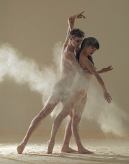 Two ballet dancers perform dance against background of white flour cloud in air.