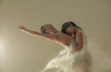 Two ballet dancers dance against white flour cloud in air.