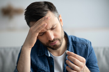 Closeup of sad man having headache, holding pill