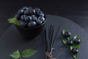 Arándanos en un recipiente negro decorado con hojas verdes sobre fondo negro en pizarra redonda